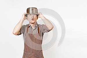 Fun man in striped apron with silver stainless glossy aluminium empty stewpan, pan or pot on head isolated on white