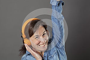 Fun middle aged woman listening to music with arms raised