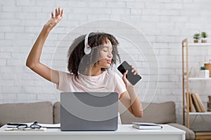 Fun music break and vocals app. Cute african american woman in headphones with closed eyes enjoys and sings at