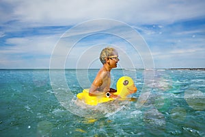 Fun at ocean - boy in sunglasses swim with inflatable duck