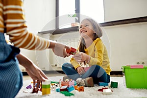 Fun and play all day. Caucasian little girl spending time with african american baby sitter, playing with construction