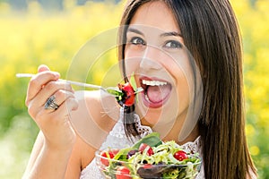 Fun portrait of cute girl eating green salad outdoors.
