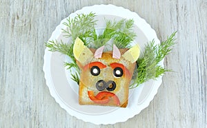 Fun sandwich with slice meat sausage, cheese, bell pepper, olives, dill on plate . funny baby food in the form of an animal face.