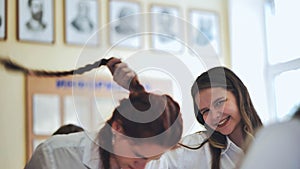 Fun schoolgirls in the classroom. Girl playing with her friend& x27;s pigtail.