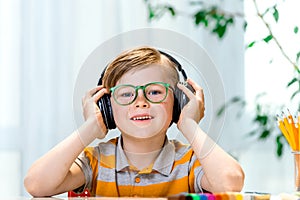 Fun smilling young child enjoying rhythms in listening to music on headphones. Smiling blond boy with freckles in yellow