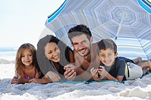 Fun in the sun. A happy family smiling at the camera while lying under an umbrella at the beach.