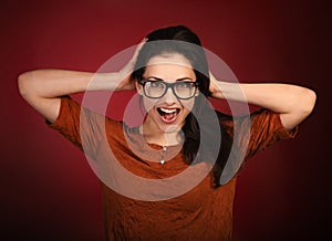 Fun surprising shouting smiling happy woman with open mouth in eye glasses and holding the hands the head in casual orange t-shirt
