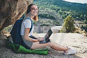 Fun tourist girl with glasses and headphones using digital tablet device relax in nature outdoor, hipster woman with backpack