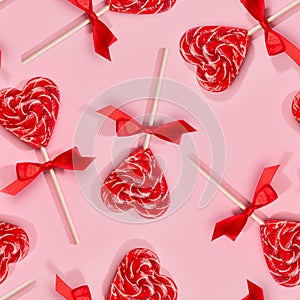 Fun valentine`s day background - sweet red lollipops hearts with bows on pastel pink as decorative seamless pattern.