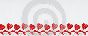 Fun valentines day background - sweet red lollipops hearts with bows on white wood board as decorative seamless border for banner.