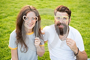 Fun Valentines props. Bearded man and sexy girl smiling with fancy party props on green grass. Funny couple holding