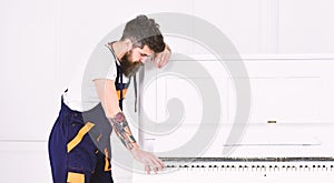 Fun at work. Handsome mover playing pianoforte isolated on white background. Side view bearded guy leaning on piano