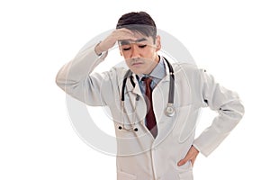 Fun young brunette man doctor in white uniform with stethoscope thinking isolated in studio