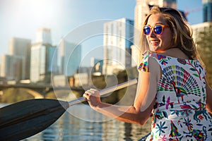 Fun young woman in sunglasses smiling,  enjoying life and having fun in boat on a river next to a city skyline