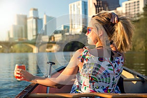 Fun young woman in sunglasses smiling,  enjoying life and having fun in boat on a river next to a city skyline