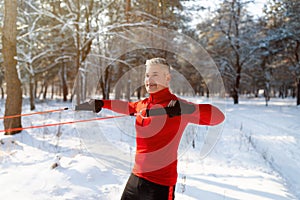 Functional workout. Strong mature sportsman exercising with bodyweight resistance straps at park on cold snowy day
