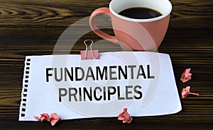 FUNDAMENTAL PRINCIPLES - words on a white sheet on a wooden brown background with a cup of coffee and a pen