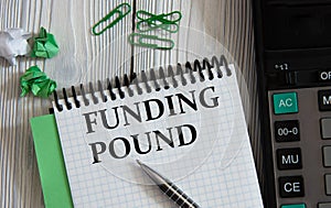FUNDING POUND - words on a white notepad on the background of a calculator, paper clips