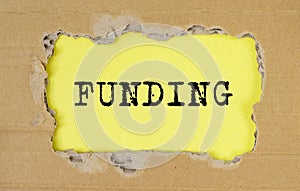 FUNDING word written on yellow table through torn craft paper