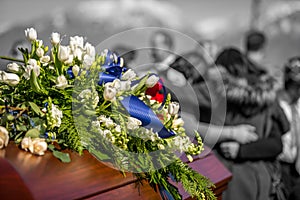 Funeral Casket In Color and Focus, With Family Mourning in Background Out of Focus and In Black And White