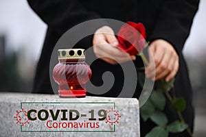 Funeral ceremony devoted to coronavirus victims. Woman holding rose near tombstone with candle outdoors