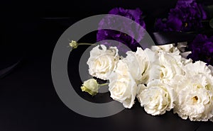 Funeral flowers of white and purple eustoma on a black background. Copy space.