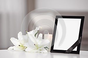 Funeral photo frame with black ribbon and lilies on white table indoors