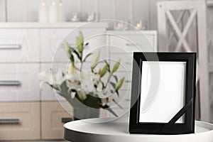 Funeral photo frame with black ribbon on tabl