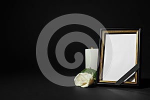 Funeral photo frame with ribbon, white rose and candle on table against black background. Space for design