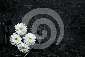 Funeral symbols. White flower near black ribbon on black background top view copy space