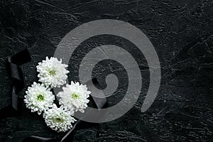 Funeral symbols. White flower near black ribbon on black background top view copy space photo