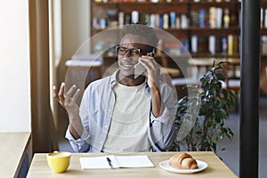 Funky African American guy making call on smartphone while studying in coffee shop