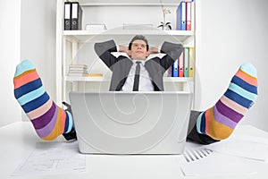 Funky socks. Happy businessman in funky socks sitting at his working place and holding head in hands