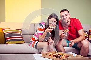 Funky young couple eating pizza on a couch