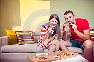 Funky young couple eating pizza on a couch