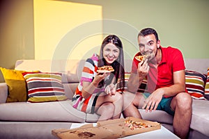 Funky young couple eating pizza on a couch