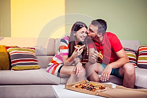 Funky young couple eating pizza on a couch