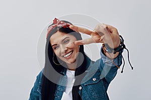 Funky young woman in bandana looking at camera and gesturing while standing against grey background