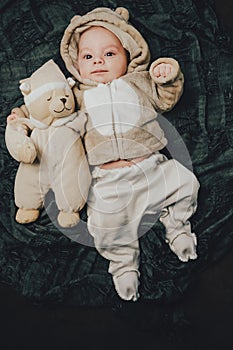 Funny 2 month old baby boy in cute costume lying on back with soft bear toy.