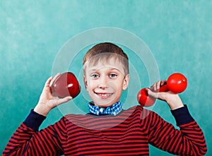 Funny active schoolboy excercising holding an apple and a dumbbell