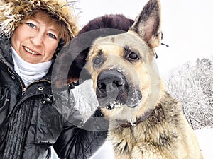 Funny Adult girl with shepherd dog in fur caps taking selfie in winter cold nature. Middle aged woman, big pet in