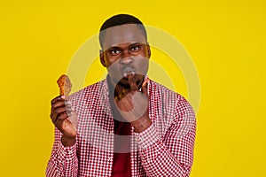 Funny african american man eating fried chicken leg in studio yellow background