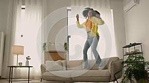 Funny African American woman happy girl at home dancing jumping have fun fooling joy testing comfortable soft couch cozy