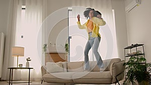 Funny African American woman happy girl at home dancing jumping have fun fooling joy testing comfortable soft couch cozy