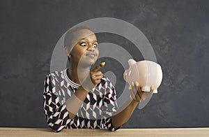 Funny african american woman punishing waving her finger to the piggy bank in her hand.