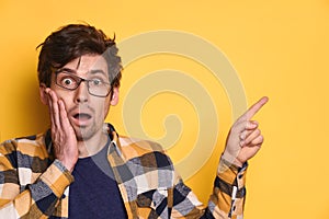 Funny amazed guy pointing at copy space on yellow studio background