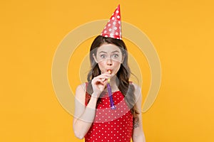 Funny amazed young brunette woman girl in red summer dress, birthday hat posing isolated on yellow wall background