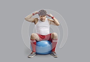 Funny angry chubby man sitting on fitness ball and getting ready for gym workout