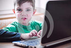 Funny angry little boy using laptop, close-up