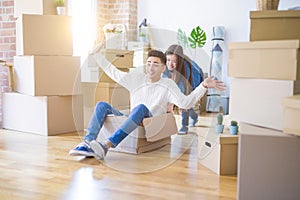 Funny asian couple having fun, riding inside cardboard box smiling happy, very excited moving to a new house